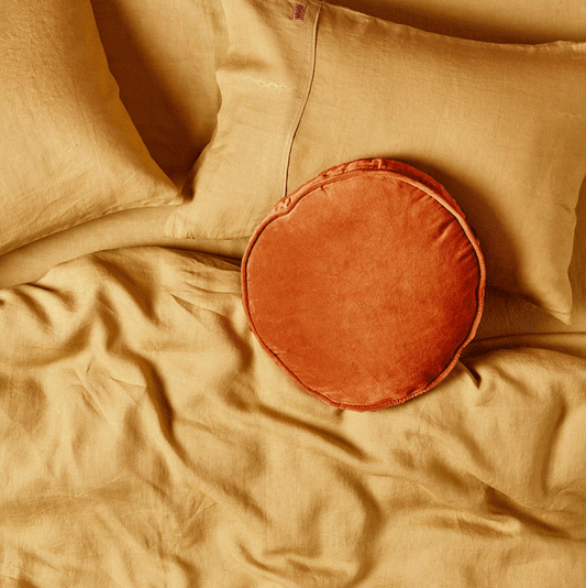 Kip & Co American Mustard Linen Pillowcase Set on a bed with a deeper mustard round velvet cushion